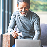Happy older man using his credit card to make a purchase on his laptop.
