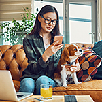 Smiling lady checking cell phone while sitting on couch with dog.